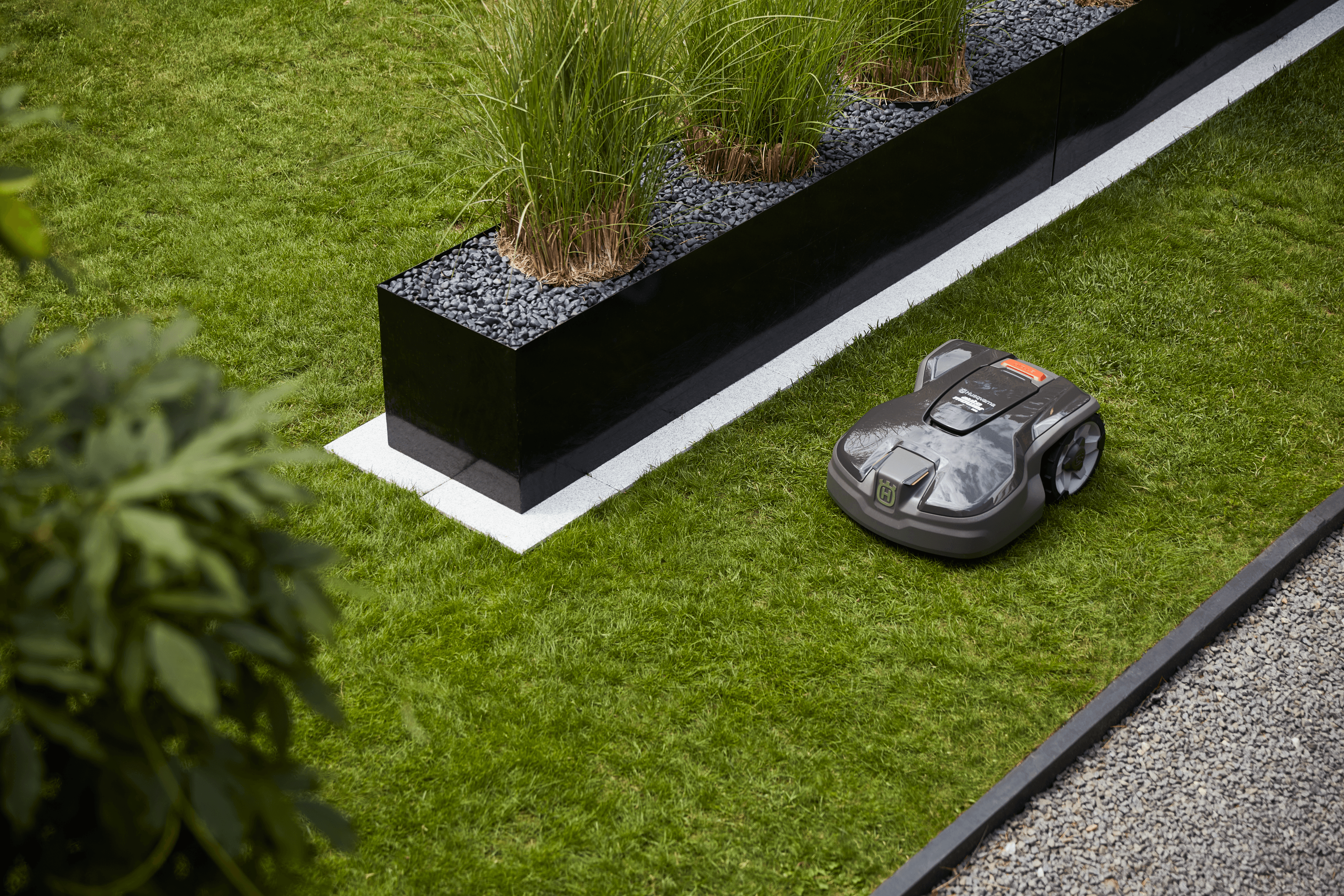 Automower sitting in grass patch in backyard with family cooking bbq in background